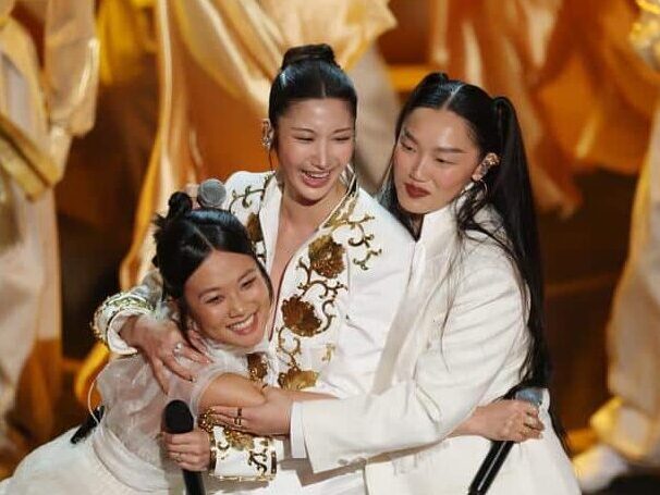 KPop Demon Hunters singers REI AMI, EJAE, and Audrey Nuna embrace after Oscars "Golden" performance.