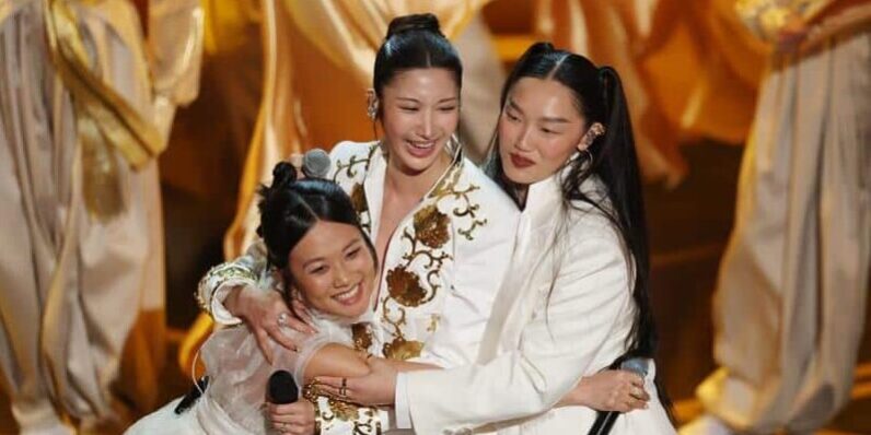 KPop Demon Hunters singers REI AMI, EJAE, and Audrey Nuna embrace after Oscars "Golden" performance.