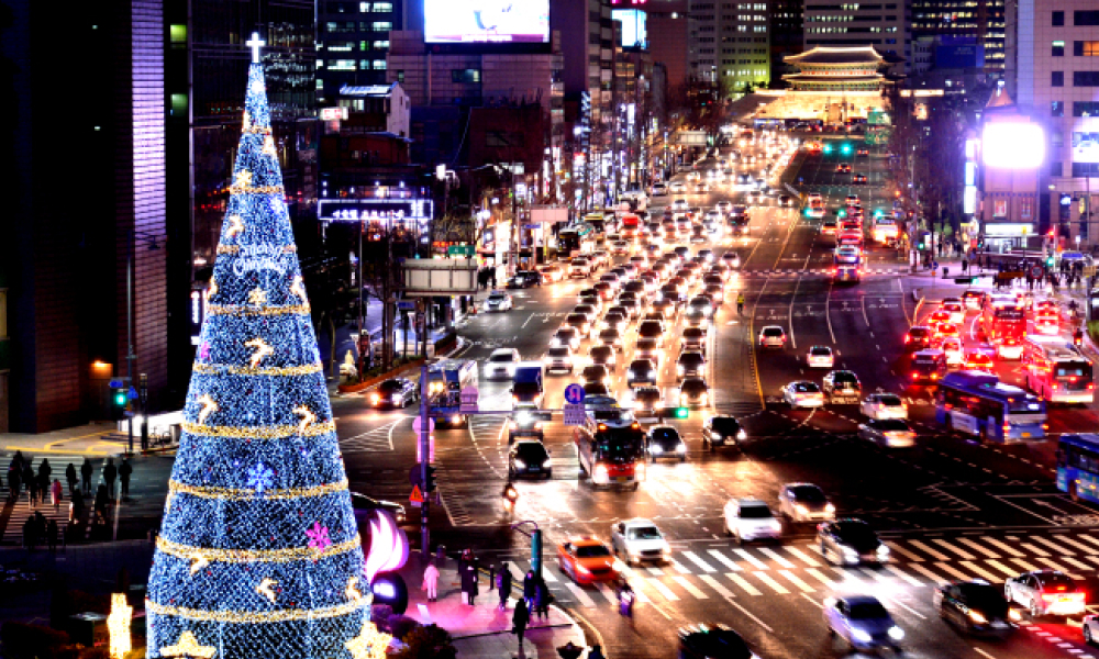A view of Seoul’s busy streets at night with a Christmas tree in the front and Gyeongbokgung Palace in the back.