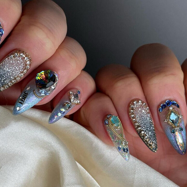 Blue and silver crystals and glitter adorn a very detailed Korean manicure with pointed tips.
