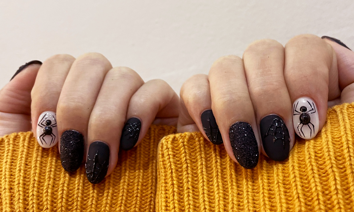 A matte and shiny Halloween and spider themed nail design full of black glitter, shiny spider webs, and two huge spiders on a white polished background.