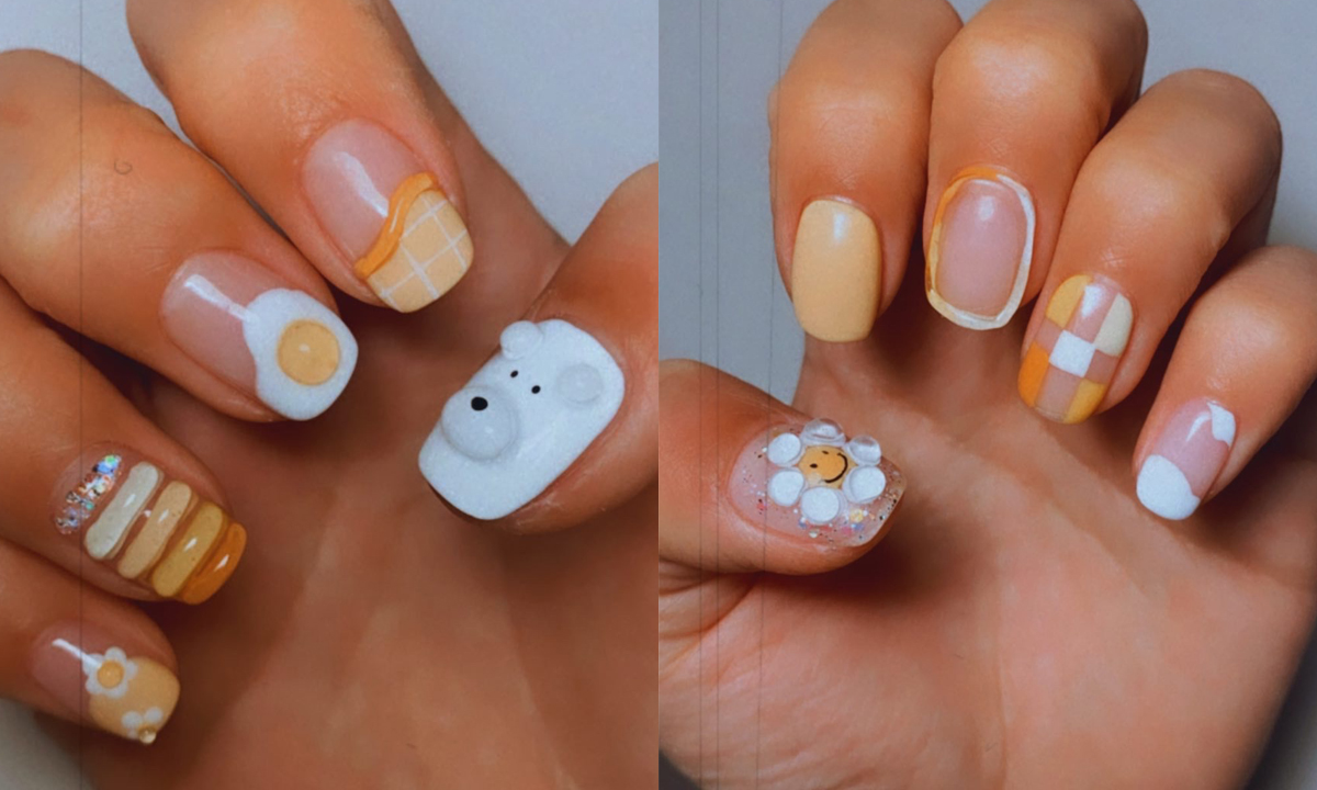 A cute yellow and white Korean manicure where every nail is a different design. There is a bear’s face, a flower, and other 3D elements.