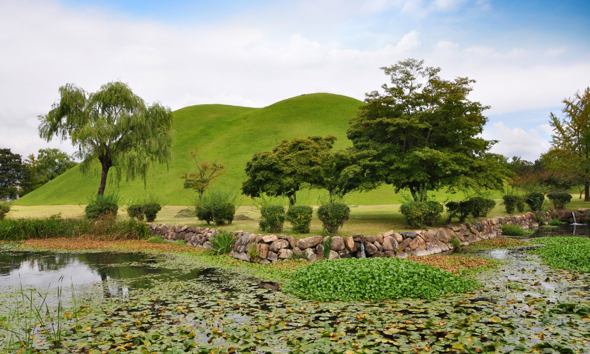 A lush and green pond and image of Gyeongju's Daereungwon Tomb and Tumuli Park.