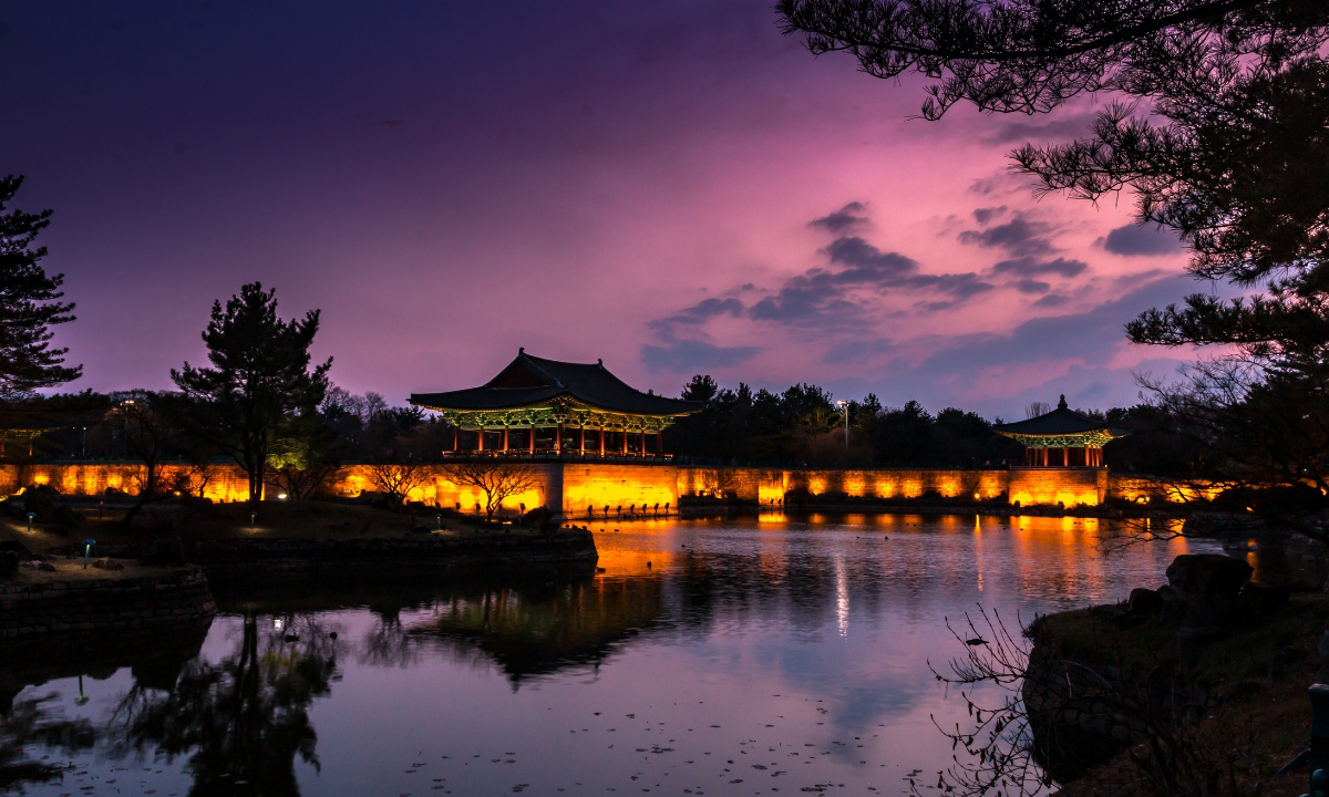 The sun sets a pink and purple hue as Donggung Palace begins to light up. The reflection of the buildings and sky can be seen in Wolji Pond.