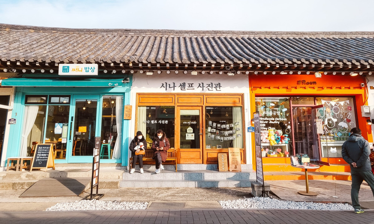A blue cafe, tan photo studio, and orange shop are located side-by-side under a hanok style roof.