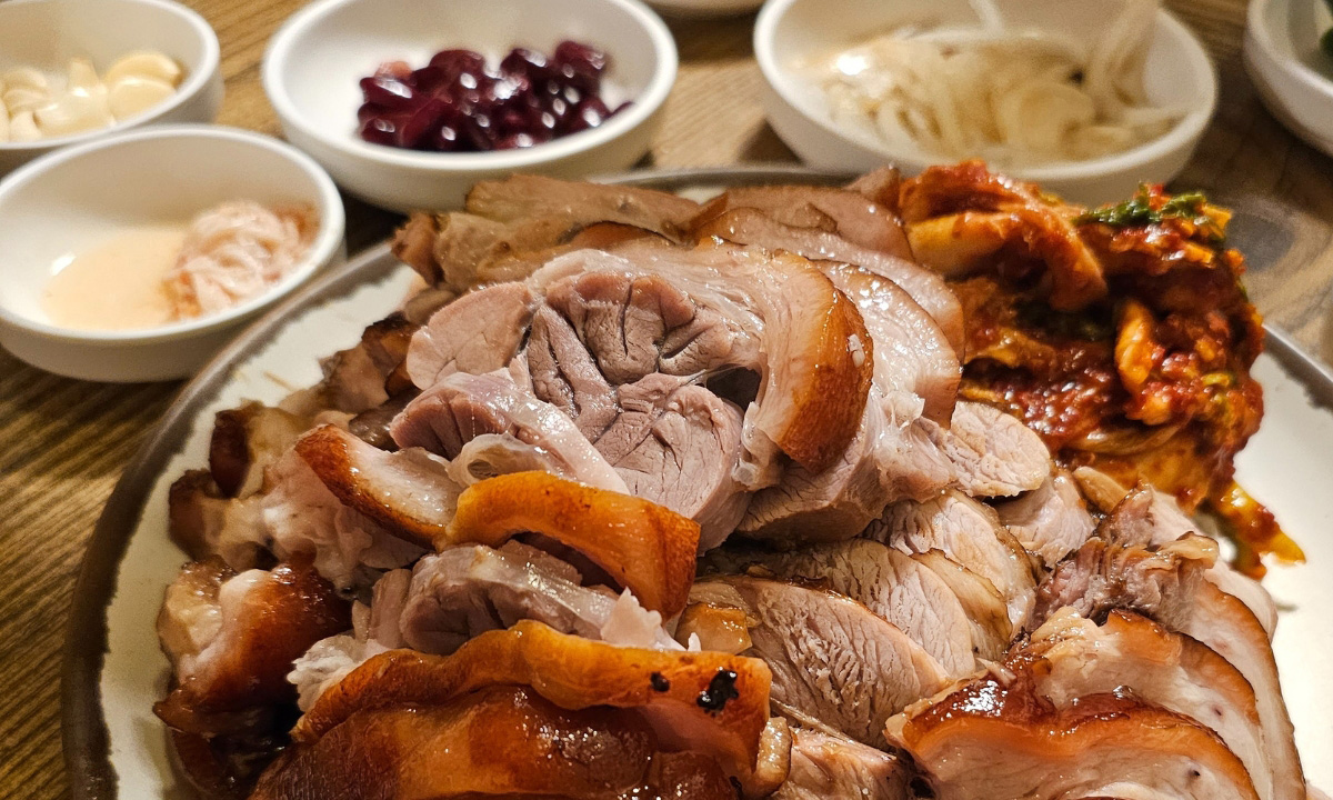 A close up shot of a large plate of pig trotters with blurred out Korean side dishes in the background.