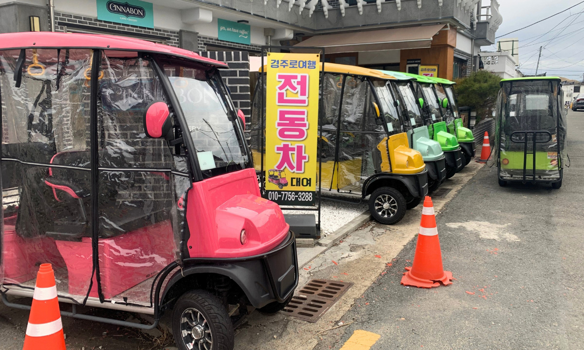 A row of pink, green, mint, and yellow golf carts are parked on the side of the road in Gyeongju’s Hwanglidan-gil (황리단길).