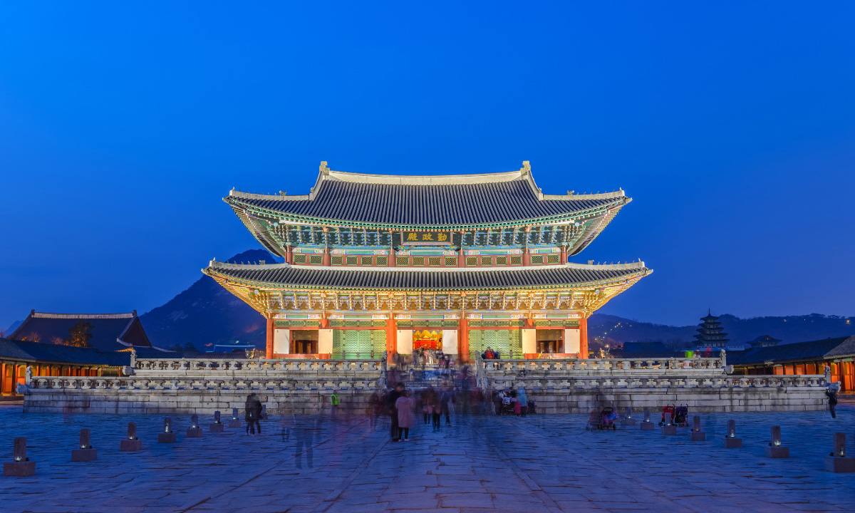The Gyeongbokgung Palace's famous entrance building lit up at night amidst a bright blue evening sky.