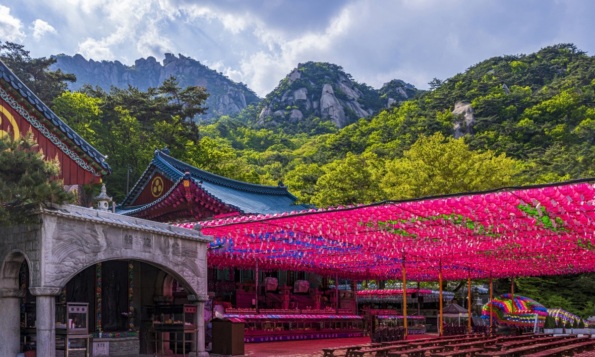 The Doseona Temple is on the left of the frame with a large blanket of hanging mostly pink lanterns. The Bukhansan Mountain is in the background.