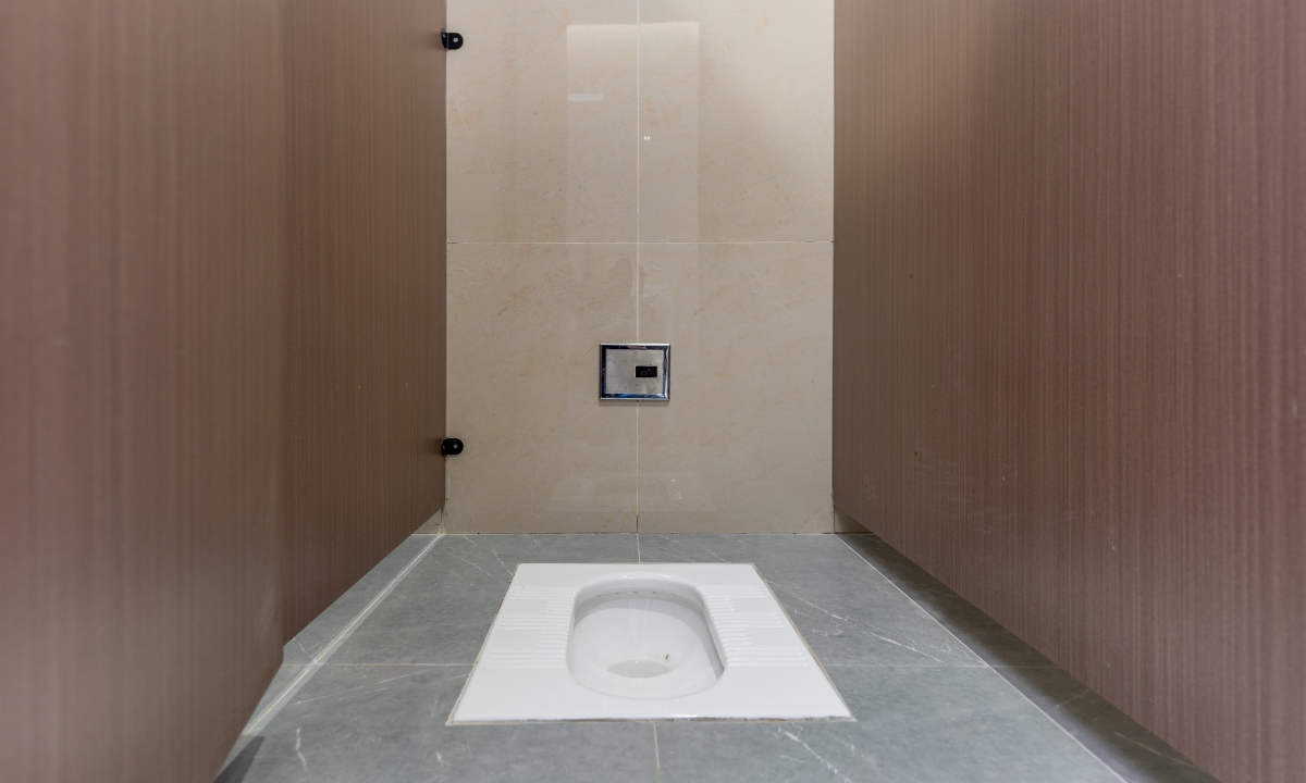 A view of a white squatting toilet with clean marble and stone tiles and wood panels.