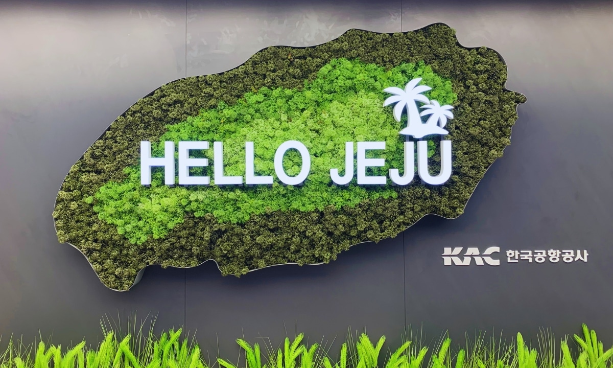 A large sign reading "Hello Jeju" on a vibrant, lush green backdrop depicting the bird’s eye view outline of Jeju Island.