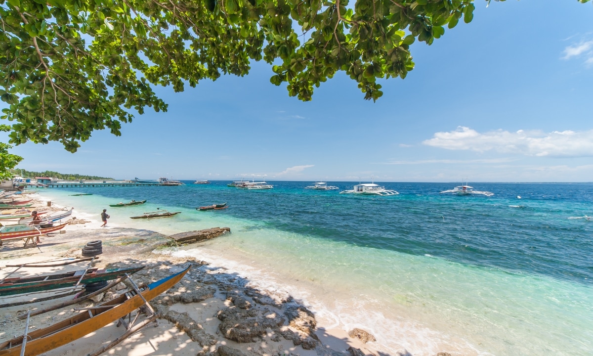 An angled view of the canoes and kayaks on Liloan’s beachfront with bright clear skies and vibrant blue waters.