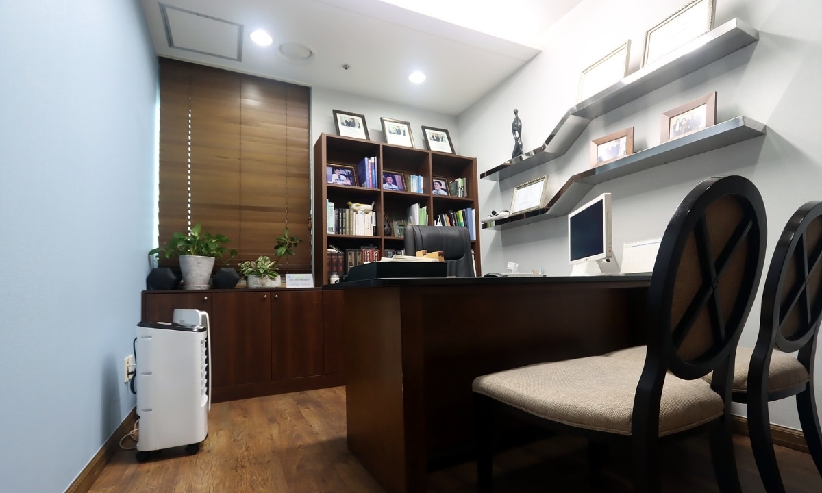 A wide angle view of Theme Dermatologist's Seoul office with dark wood furniture, photos on the walls, and bright ceiling lights.
