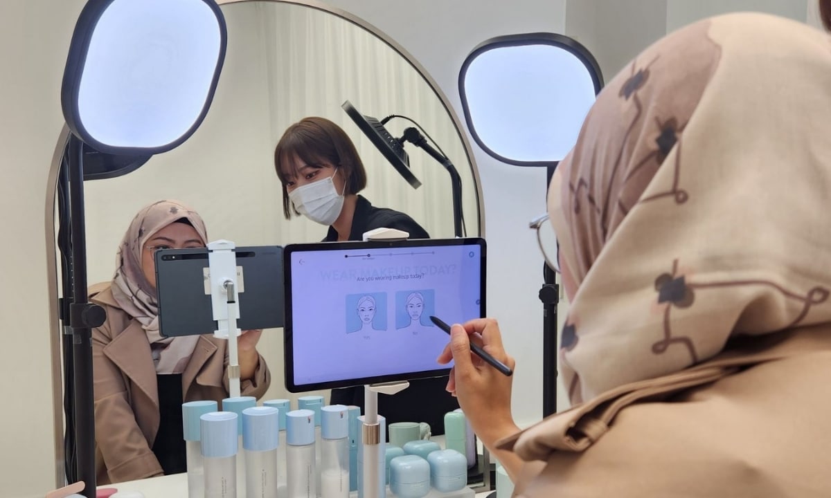 A woman with a muted purple floral hijab sits in the foreground looking at a Laneige’s tablet with a Korean Laneige consultant.