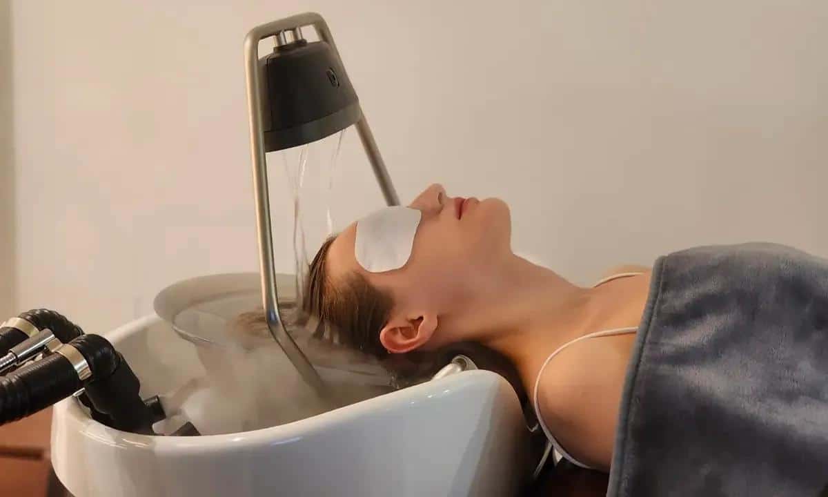 A woman lays down with spa eye patches over eyes, and her hair in a relaxing scalp spa bath.