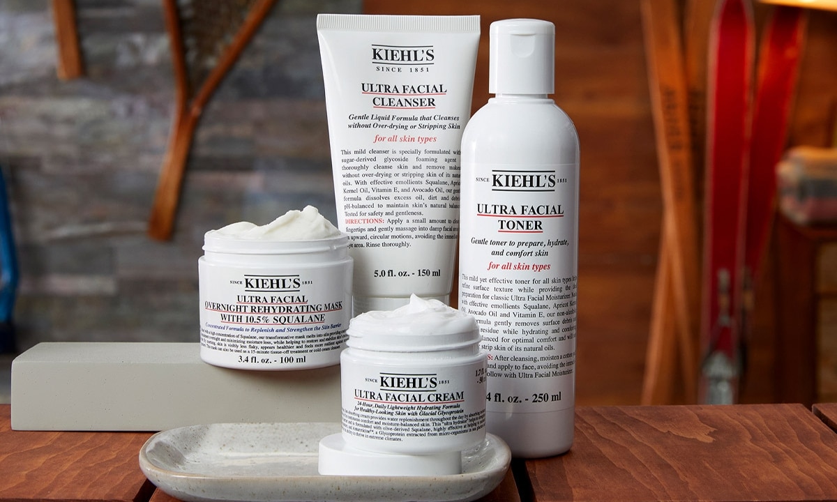 A selection of Kiehl's skincare products, including creams, cleansers, and travel-size bottles on a wooden surface.