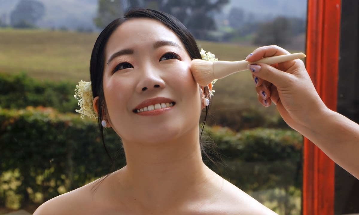 Bride smiling as a makeup artist applies final touches before the wedding ceremony.
