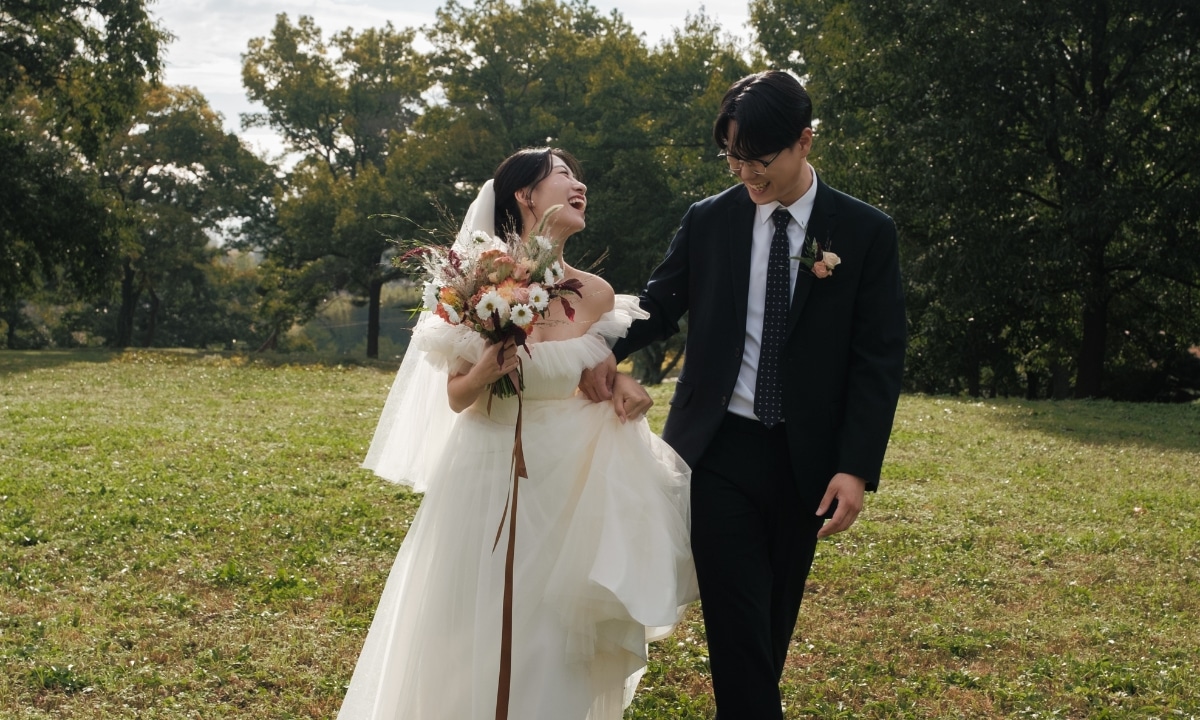 Bride and groom walking hand-in-hand through a quiet park smiling and laughing during a wedding photo shoot.