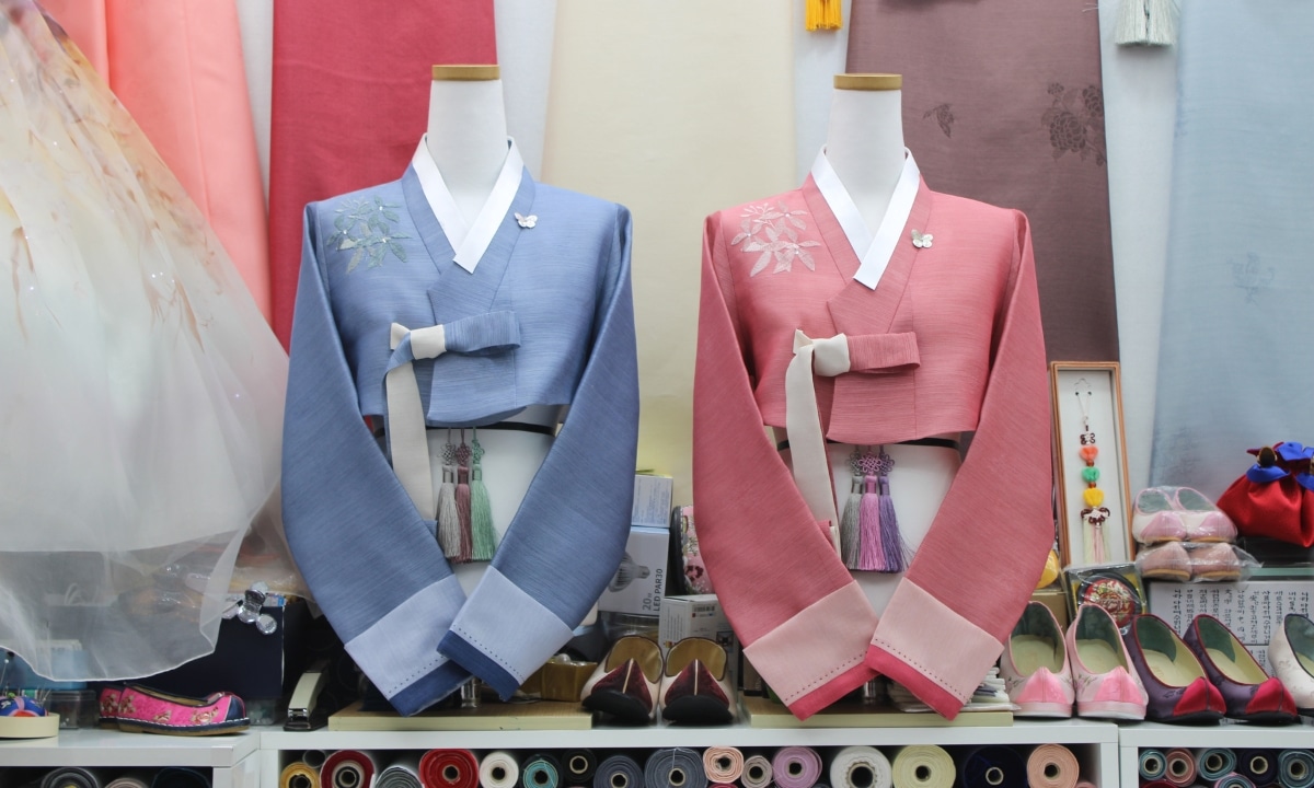 Blue and pink hanboks displayed on mannequins inside a hanok-style shop in Korea.