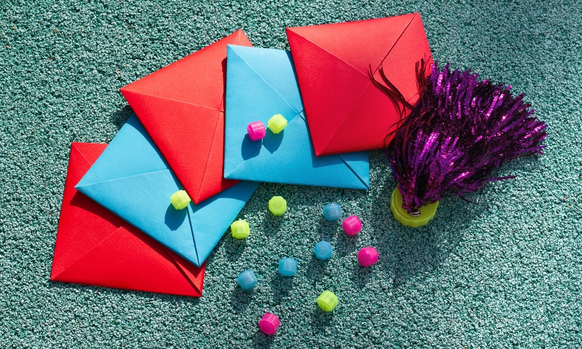 Brightly colored envelopes, beads, and a purple pom-pom scattered on a textured blue surface, suggesting a festive or playful activity.