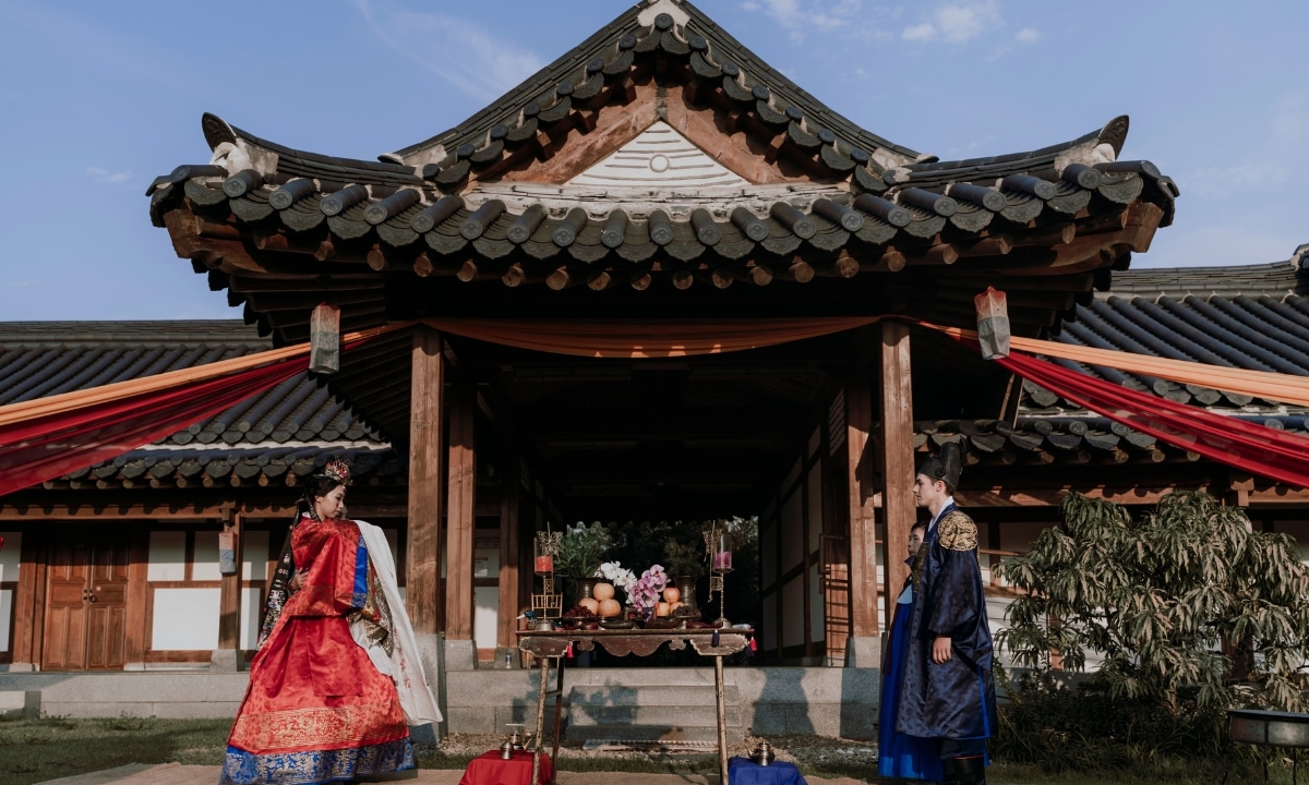 Bride and groom standing in front of a hanok, appear to be moments away from bowing to one another.