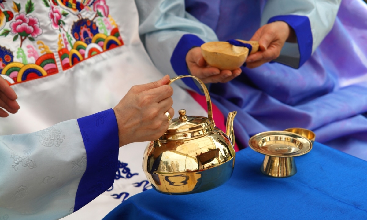 Close-up shot of a traditional Korean wedding ritual where the couple exchanges drinks in a gourd and copper cup.