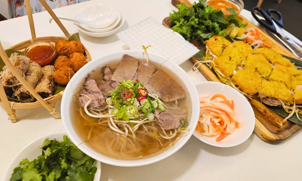 A bowl of Vietnamese pho with herbs, fried appetizers, and dipping sauce.