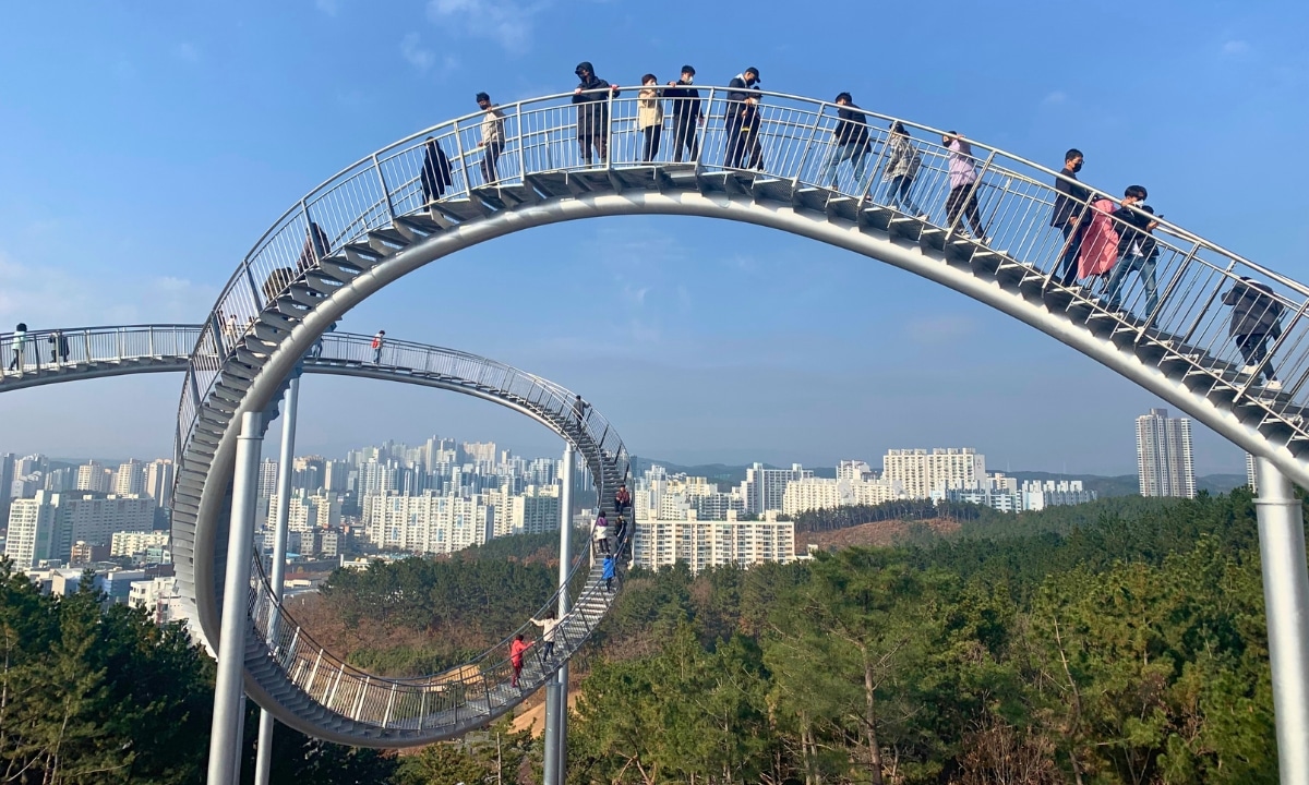 Tourists walking across the elevated Pohang Space Walk bridge above the forest.