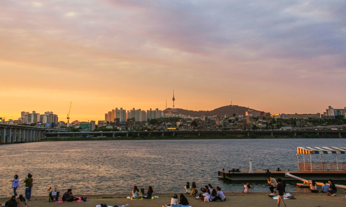Scenic view of people enjoying a sunset picnic by the Han River in Seoul, a favorite way to relax during warm Korean summer evenings.