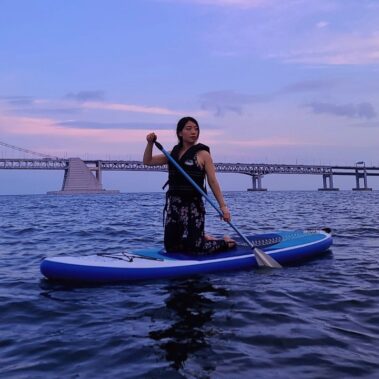Swimmer wearing modest swimwear paddle boards in the sea under a sunset bright sky.
