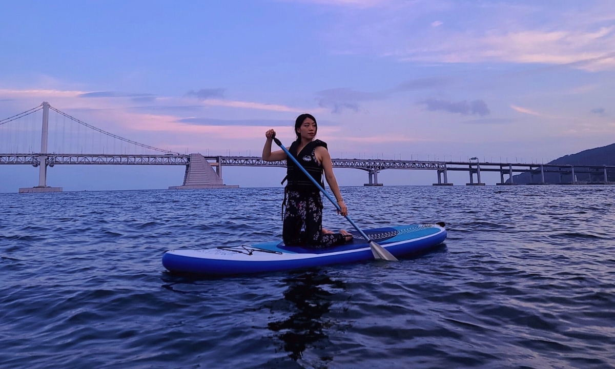 Swimmer wearing modest swimwear paddle boards in the sea under a sunset bright sky.