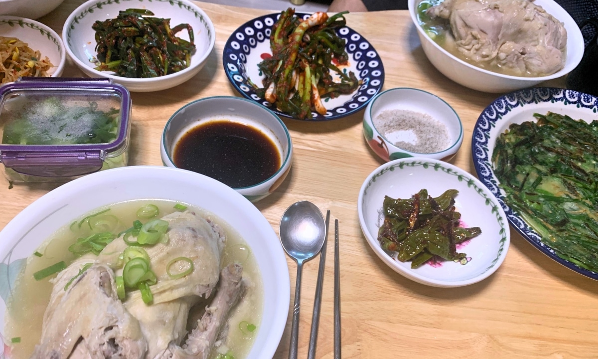 A hot bowl of samgyetang surrounded by traditional Korean side dishes, served as a restorative meal during the peak of Korean summer.